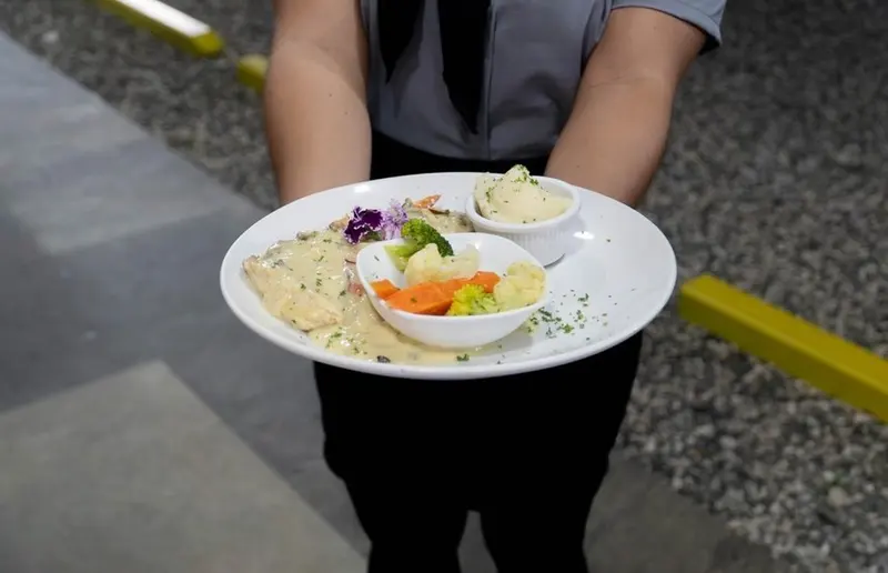 Pescado en salsa blanca con vegetales, servido por el personal del restaurante