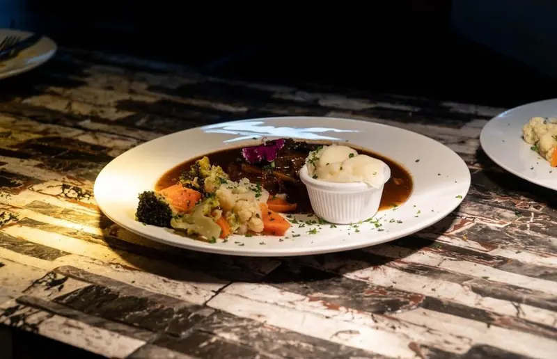 Carne en salsa oscura con puré de papa y vegetales sobre mesa de mármol