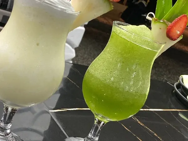 Dos cócteles tropicales, uno blanco y otro verde, decorados con piña